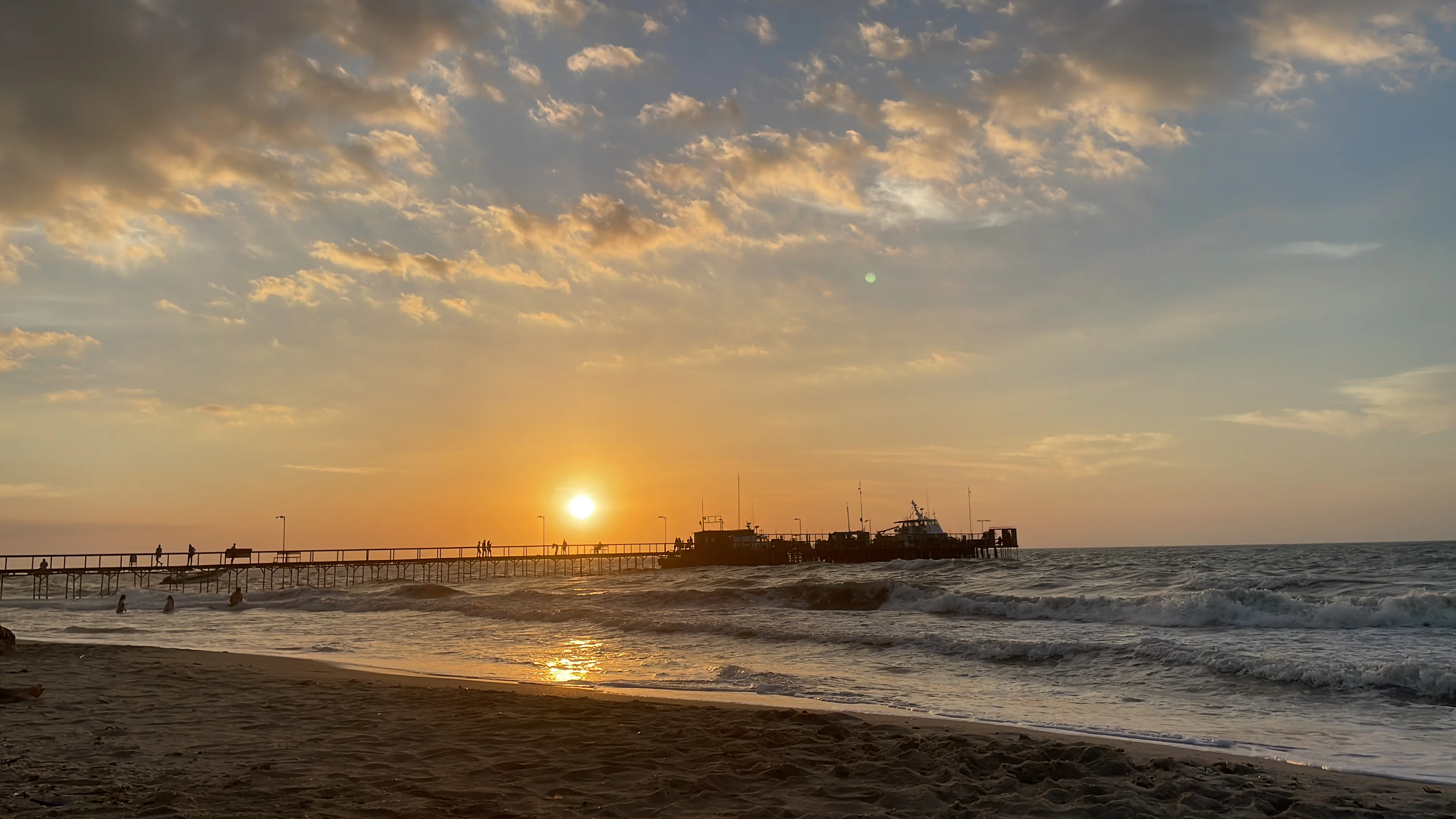 Atardecer sobre el mar Caribe desde la playa de Riohacha, con el muelle turístico recortado contra el sol